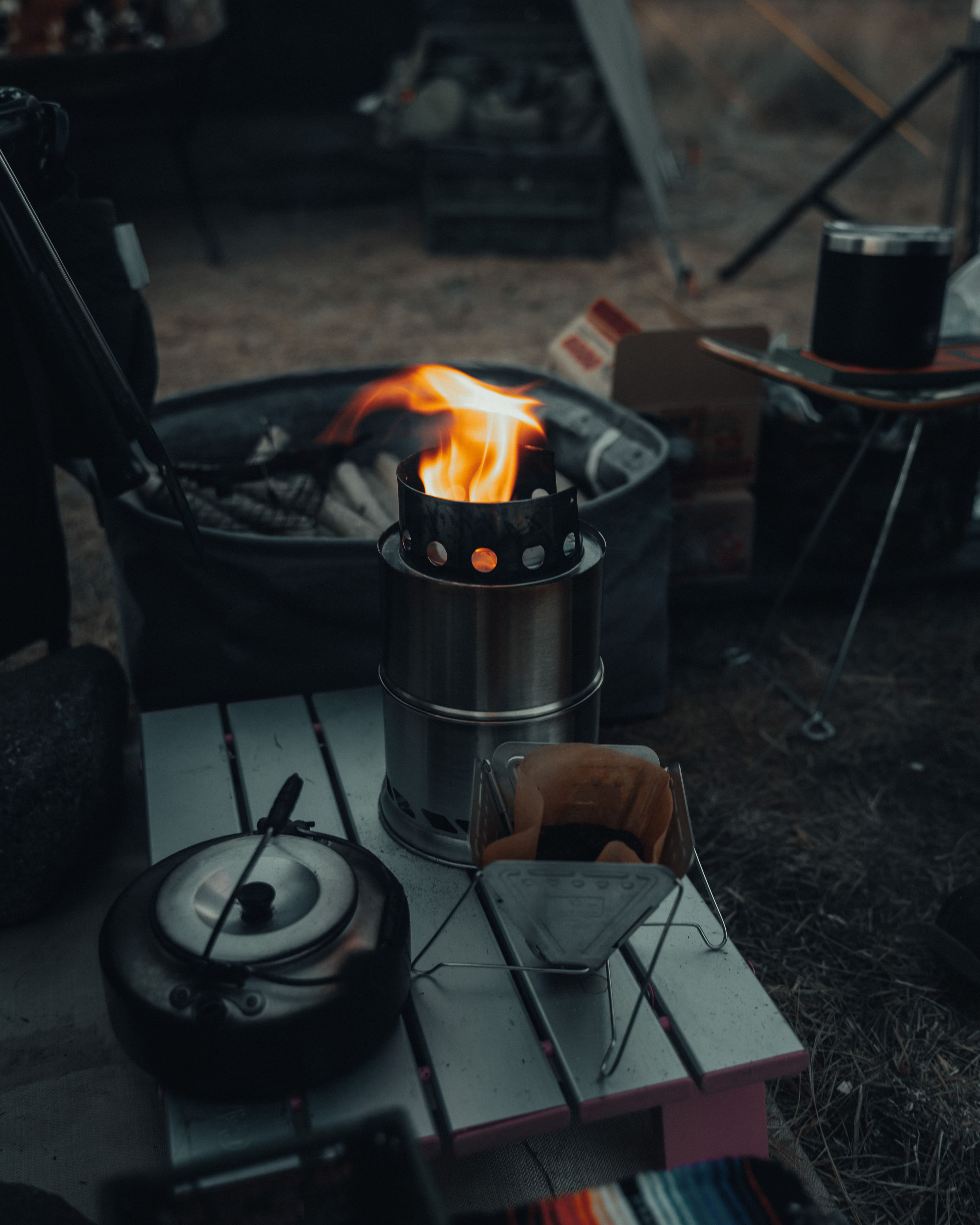 A portable wood-burning camp stove boiling water at dusk, part of an internet and grid outage survival kit